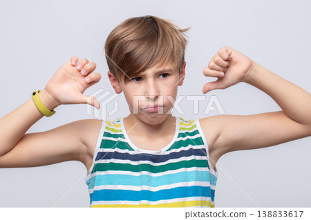 Young boy expresses disappointment with thumbs down gesture against a light background Young boy expresses disappointment with thumbs down gesture against a light background 138833617