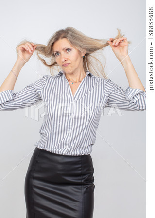 Woman with long hair playfully pulling strands while posing in a stylish outfit against a neutral background Woman with long hair playfully pulling strands while posing in a stylish outfit against a neutral background 138833688
