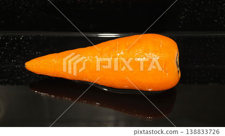Bright orange carrot on a black surface with shiny texture in a kitchen setting Bright orange carrot on a black surface with shiny texture in a kitchen setting 138833726