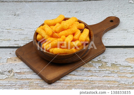 Cheese flavored corn puffs in wooden bowl on rustic wood background, crunchy savory cheese snacks Cheese flavored corn puffs in wooden bowl on rustic wood background, crunchy savory cheese snacks 138833835
