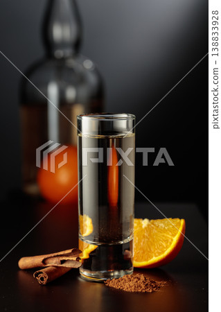 Mexican gold tequila with an orange slice and cinnamon on a black table. 138833928