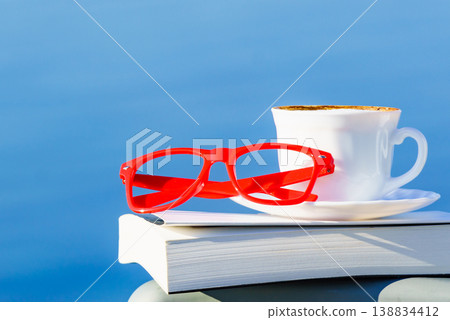 Coffee cup, book and glasses against blue sea. 138834412