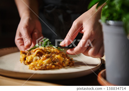 Serving homemade lasagna with fresh garnish in cozy kitchen 138834714