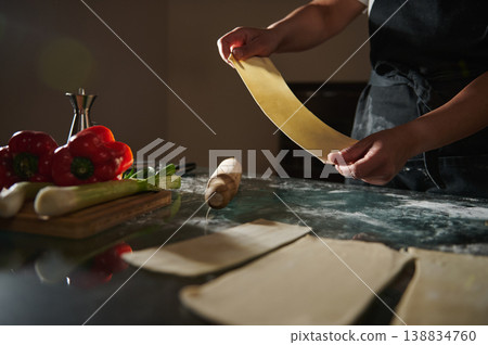 Woman stretching fresh dough sheet for homemade baking in kitchen Woman stretching fresh dough sheet for homemade baking in kitchen 138834760