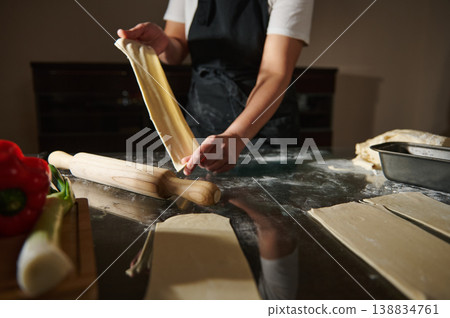 Woman holding elastic dough sheet while preparing homemade pastry Woman holding elastic dough sheet while preparing homemade pastry 138834761