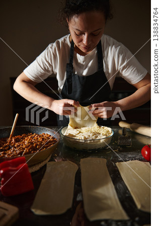 Woman preparing layered pie with dough and filling on kitchen table 138834764