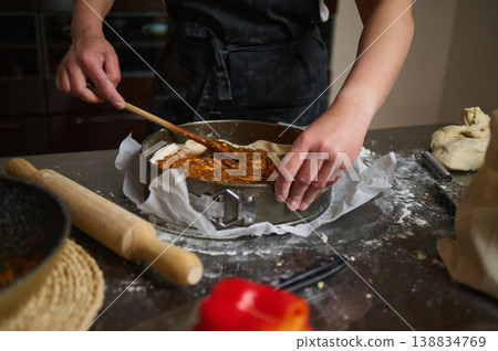 Spreading sauce into lasagna baking dish with wooden spoon 138834769