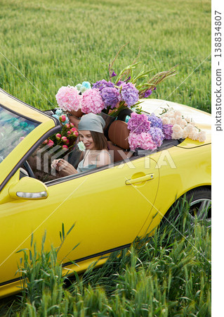 Smiling woman sits in yellow convertible surrounded by colorful flowers Smiling woman sits in yellow convertible surrounded by colorful flowers 138834807