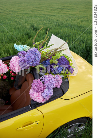 Smiling woman sits in yellow convertible surrounded by colorful flowers Smiling woman sits in yellow convertible surrounded by colorful flowers 138834828