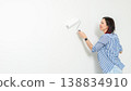 Woman painting a wall with space for text with a roller in a home renovation mockup, wearing a striped shirt and smiling while holding the roller 138834910