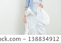 Woman in protective clothing prepares for home renovation, holding a white coverall and wearing a striped shirt in a clean indoor setting 138834912