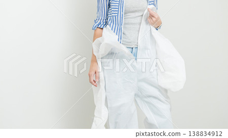 Woman in protective clothing prepares for home renovation, holding a white coverall and wearing a striped shirt in a clean indoor setting Woman in protective clothing prepares for home renovation, holding a white coverall and wearing a striped shirt in a clean indoor setting 138834912