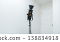 Studio spotlight on a tripod in a minimalistic interior setting with a white wall and a closed door in the background 138834918