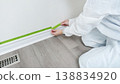Person applying painter's tape along baseboard in preparation for painting a wall, wearing protective coveralls in a clean interior space 138834920