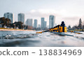 College students rowing in a team on a river, city skyline visible in the background with tall buildings and clear blue sky 138834969