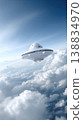 Futuristic flying saucer spacecraft hovering above fluffy white clouds in a clear blue sky, showcasing advanced design and technology 138834970