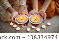 Two hands holding decorative diyas with lit candles, surrounded by additional candles on a soft surface during Diwali celebration in India 138834974