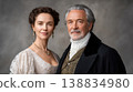 Elegant couple in historical attire poses for portrait, woman in lace dress and man in formal coat with a neutral backdrop 138834980