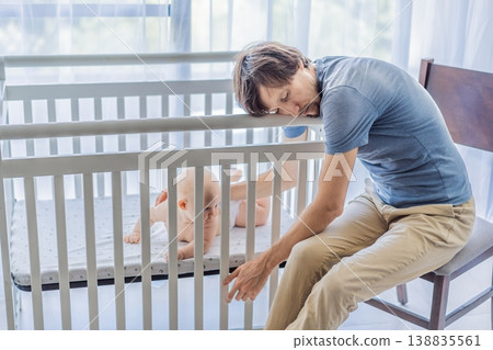 Tired father sitting by baby crib at home watching sleeping infant. Exhausted dad caring for newborn at night. Parenting fatigue, childcare responsibility, love and real family life concept Tired father sitting by baby crib at home watching sleeping infant. Exhausted dad caring for newborn at night. Parenting fatigue, childcare responsibility, love and real family life concept 138835561