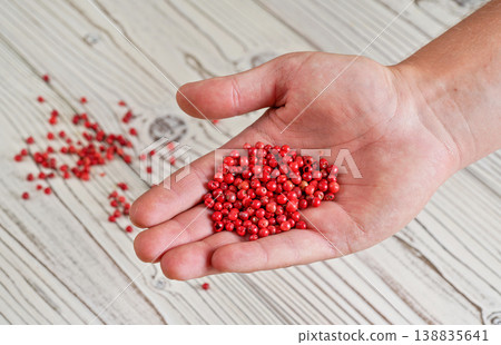 Red or Pink peppercorn in young man hand, more scattered on white boards desk below, closeup photo Red or Pink peppercorn in young man hand, more scattered on white boards desk below, closeup photo 138835641