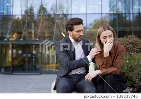Male colleague comforting a distressed businesswoman covering her face while crying due to failure, loss, or stress, sitting outside a modern office building Male colleague comforting a distressed businesswoman covering her face while crying due to failure, loss, or stress, sitting outside a modern office building 138835740