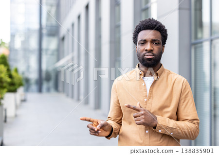 Young man standing outdoors in an urban environment, looking directly forward while confidently gesturing with both hands, indicating a choice or showing a path Young man standing outdoors in an urban environment, looking directly forward while confidently gesturing with both hands, indicating a choice or showing a path 138835901