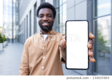Smiling man holding smartphone vertically with blank white screen for mockup, standing outdoors by a modern office building, showcasing mobile app, advertising and digital display concepts Smiling man holding smartphone vertically with blank white screen for mockup, standing outdoors by a modern office building, showcasing mobile app, advertising and digital display concepts 138835903