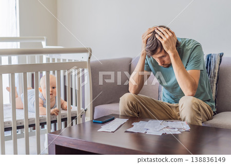 Father sitting on sofa calculating monthly expenses with receipts while baby lies in crib nearby at home. Stressed dad managing budget and childcare. Financial pressure and parenthood concept Father sitting on sofa calculating monthly expenses with receipts while baby lies in crib nearby at home. Stressed dad managing budget and childcare. Financial pressure and parenthood concept 138836149