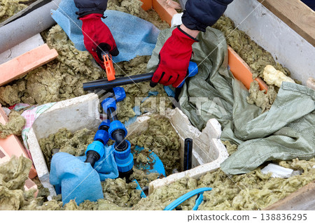 Well contractor using ratchet pipe cutter working on distribution manifold with service lines in well pit. Well contractor using ratchet pipe cutter working on distribution manifold with service lines in well pit. 138836295