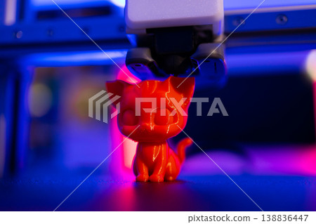 A bright red, cartoon-style cat figurine is being printed by a 3D printer with blue and pink neon lighting A bright red, cartoon-style cat figurine is being printed by a 3D printer with blue and pink neon lighting 138836447
