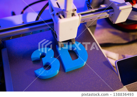 A 3D printer is actively creating the blue letters '3D' on its build plate, illuminated by purple light A 3D printer is actively creating the blue letters '3D' on its build plate, illuminated by purple light 138836493