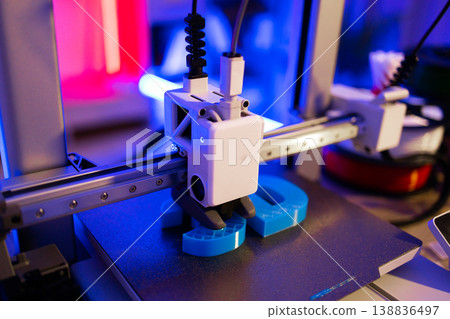 A modern 3D printer is actively creating a blue object layer by layer with vibrant neon lighting 138836497