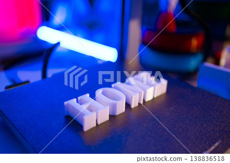 White 3D printed letters spelling out HOME sit on a dark textured surface illuminated by blue and pink neon lights 138836518