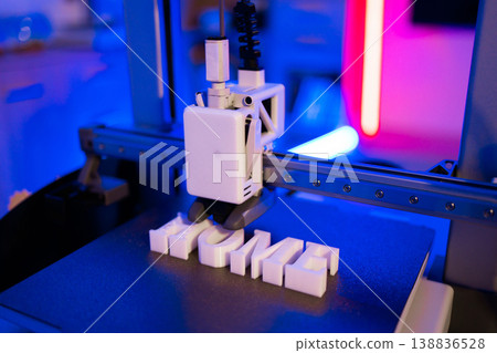 A modern 3D printer is actively creating the word HOME in white plastic letters on its build plate with vibrant blue and pink lighting 138836528