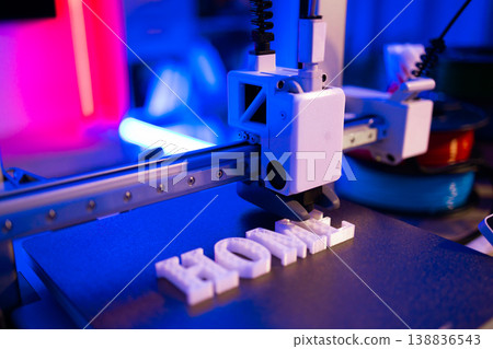 A 3D printer is actively creating the word HOME in white plastic letters on a dark surface with vibrant blue and pink lighting A 3D printer is actively creating the word HOME in white plastic letters on a dark surface with vibrant blue and pink lighting 138836543
