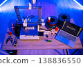 A 3D printer is actively creating the word HOME while filament spools and tools are laid out on a wooden desk 138836550