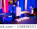 A 3D printer is actively creating white plastic letters on its build plate under vibrant blue and pink lighting 138836553