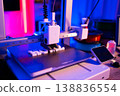 A modern 3D printer is actively creating white plastic letters on its build plate with vibrant neon lighting 138836554