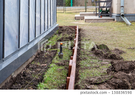Digging Trench for Wooden Raised Garden Bed Installation Along Greenhouse Side Digging Trench for Wooden Raised Garden Bed Installation Along Greenhouse Side 138836598