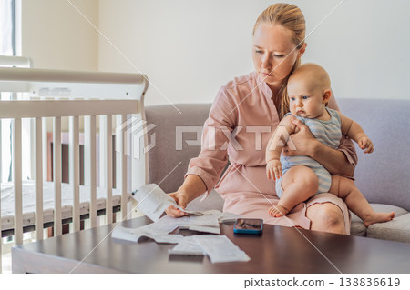 Mother sitting on sofa holding baby while calculating monthly expenses with receipts at home. Stressed mom managing budget and childcare. Financial stress, parenthood and real life concept 138836619