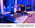 A 3D printer is actively creating the word HOME in white plastic letters on its build plate with a laptop displaying the same word in the background 138836656