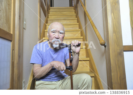 一位留著鬍子的老人拄著拐杖在室內樓梯上做復健運動。 138836915