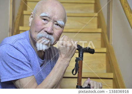 An elderly man with a beard is using a cane to do rehabilitation exercises on the indoor stairs. An elderly man with a beard is using a cane to do rehabilitation exercises on the indoor stairs. 138836916