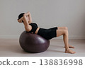 Slim caucasian woman with dark hair performing abdominal exercise on large fitness ball in modern pilates studio. Trendy sportswear and controlled movement highlight core strength balance and ifestyle 138836998