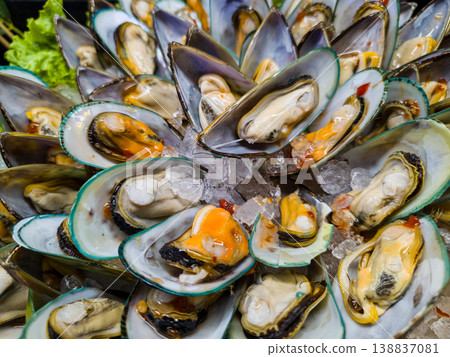 High angle view of cooked green mussels on shells arranged in a circle on ice. Seafood platter on display at a market. Healthy mediterranean food. 138837081