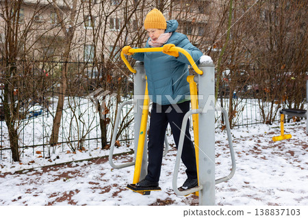 Senior woman exercising on outdoor fitness machine in winter Senior woman exercising on outdoor fitness machine in winter 138837103