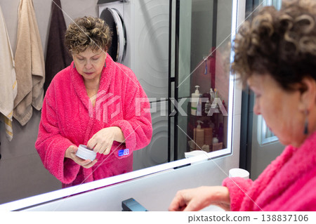 Applying under eye patches mature woman skincare routine in bathroom 138837106