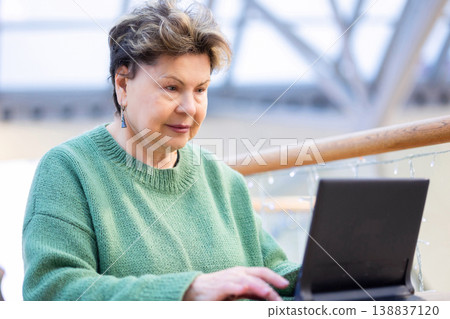 Mature woman working on laptop in shopping mall interior Mature woman working on laptop in shopping mall interior 138837120