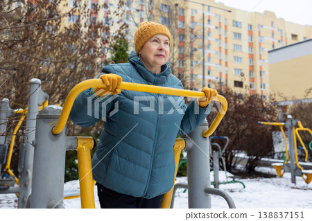 Senior woman exercising on outdoor fitness machine in winter Senior woman exercising on outdoor fitness machine in winter 138837151