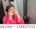 Applying under eye patches mature woman skincare routine in bathroom 138837153